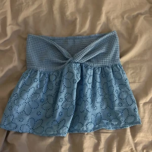 Ljusblå topp med broderade blommor - Supersöt ljusblå top  med virkad volang och twistad detalj framtill. Toppen har ett broderat blommönster på det tunna tyget och ger en riktigt fräsch vibe. Perfekt för varma dagar.