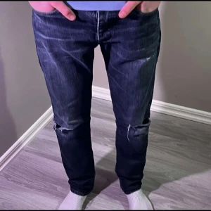 Mörkblå jeans med slitna knän - Snygga mörkblå jeans med slitningar och hål vid knäna. Modellen har klassisk femficksdesign och raka ben. Jeansen har en cool tvätt med ljusare partier och är tillverkade i robust denim. Perfekt för dig som gillar en avslappnad och trendig stil.