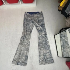 Glittriga lowrise bootcut byxor - Unika lågmidjade bootcut byxor med rutigt mönster i silver, guld och grått. Materialet har en glittrig finish och insidan är fodrad med blått tyg. Insidan på benet är lite skadat på ett ställe (se sista bilden)