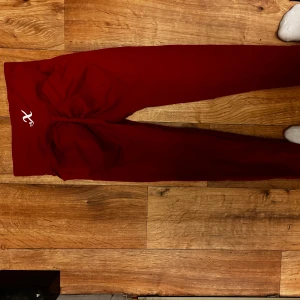 Mörkröda leggings med scrunch - Snygga mörkröda leggings med scrunch-effekt bak och ett litet vitt tryck på linningen. Stretchigt material som sitter tight och framhäver formerna. Perfekta för gymmet eller chill hemma. Färgen är djup röd och modellen är högmidjad.