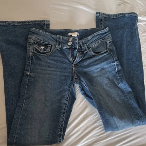 Blå jeans från Gina Tricot, stl 158 - Snygga blå jeans från Gina Tricot med klassisk femficksdesign och dubbla silverknappar i midjan. Jeansen har justerbar midja med knappresår på insidan och raka ben med lätt tvättad look. Perfekt för dig som gillar enkel och stilren denim.