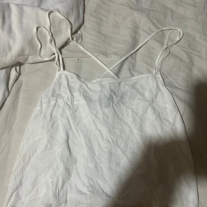 Vit linnetopp från H&M Divided - Säljer en vit linnetopp från H&M Divided i storlek 44, men skulle säga att den passar mig som använder M i toppar vanligtvis. Toppen har tunna axelband som korsas i ryggen och är tillverkad i ett lätt, krinklat bomullstyg. Varan har inga tecken på användning, har endast använt denna en gång. Perfekt för varma dagar och enkel att styla med jeans eller kjol.