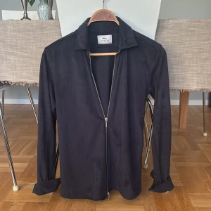 Mörkblå skjorta med dragkedja från Ciszere - Mörkblå långärmad skjorta från Ciszere i slim fit med mjuk mockakänsla. Skjortan har klassisk krage och en snygg dragkedja framtill istället för knappar, vilket ger en modern vibe. Perfekt för dig som gillar stilrena plagg med en twist. Nypris runt 1500kr