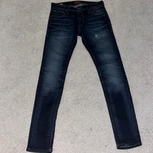 Jack & Jones Skinny Liam jeans blå - Snygga mörkblå skinny jeans från Jack & Jones, modell Liam. Klassisk femficksdesign med bruna sömmar och läderpatch bak. Stretchigt denim för skön passform och smal siluett. Perfekt för dig som gillar tajta jeans med modern look.