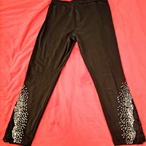 Svarta leggings med pärlor från Emery Rose - Svarta leggings från Emery Rose i storlek L, dekorerade med pärlor och spetsdetaljer vid bensluten. Stretchigt material med polyester och elastan för skön passform. Perfekt för dig som gillar att sticka ut med coola detaljer.