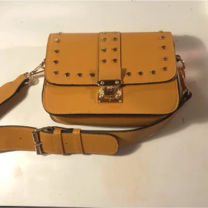 Brun axelväska med nitar och spänne - Snygg gul axelväska med bred justerbar rem och coola nitar på locket. Materialet är skinnimitation och detaljerna ger en edgy vibe. Perfekt för dig som vill sticka ut med din stil.❤️‍🔥 pris kan diskuteras