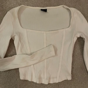 Vit ribbad korsettopp Gina Tricot XS - Säljer en vit ribbad korsettopp från Gina Tricot i storlek XS. Toppen har långärmade och en fyrkantig urringning som ger en snygg vibe. Den är croppad och har markerade sömmar framtill för en trendig look. Perfekt för dig som gillar stilrena och moderna plagg. 