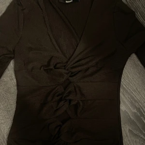 brun ribbad omlottopp med knyt - Säljer en brun ribbad omlottopp från Bik Bok med flera snygga knyt framtill. Toppen har v-ringning och lång ärm, perfekt för dig som gillar trendiga detaljer och en figurnära passform.