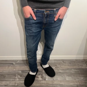 Nudie Jeans  W30 L32 - Snygga blå jeans från Nudie Jeans med klassisk orange söm på bakfickan. Modellen är slim med smal passform och normal midja. Jeansen har fem fickor, dragkedja och är tillverkade i mjukt bomullsmaterial. Perfekt för dig som gillar stilrena och moderna jeans.