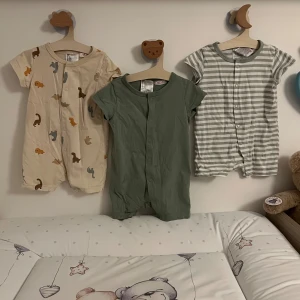 Tre bebis jumpsuit från H&M, strl 68 - Använd bara en gång.Säljer tre gulliga jumpsuit från H&M i storlek 68. Ett par är beige med djurmönster och knappar framtill, ett par är enfärgat gröna med korta ärmar och knappar, och ett par är ljusgrått och vitt randiga med knappar. Alla är i mjuk bomull, perfekta för varma dagar.