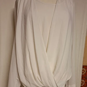 Draperad vitblus från Oasis - Säljer en stilren vit blus från Oasis i storlek 10/36. Blusen har omlottdesign framtill och långa ärmar med lätt puff vid axlarna. Materialet är mjukt och har ett snyggt fall. Perfekt för dig som gillar clean och enkel stil.