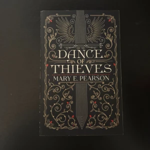 Dance of Thieves - En snyggt designad bok med guldmönster och vingar på omslaget. Perfekt för dig som gillar spännande och mystiska berättelser. Skriven av den bästsäljande författaren Mary E. Pearson.