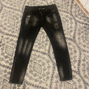 Svarta jeans Alessandro Zavetti - Svarta jeans från Alessandro Zavetti med skinny passform och slitna detaljer. Byxorna har en tvättad look med ljusare partier, små färgstänk och hål framtill. Klassisk femficksmodell och knappgylf. Har aldrig använts och säljs på grund av fel storlek. Perfekt för dig som gillar streetstyle.