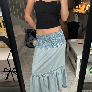 Ljusblå långkjol/klänning i denim med smock - Supersnygg ljusblå långkjol/klänning i denim med bred smock i midjan och volang nertill. Perfekt till sommaren eller resan och kan både bäras som långkjol eller klänning vilket jag älskar 💕 Använd några gånger men inga tecken på användning. Storlek S men passar även XS och M då materialet är stretchigt! 🫶🏼