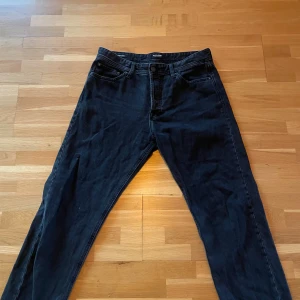 Svarta relaxed jeans från Jack & Jones - Svarta jeans från Jack & Jones, modell Relaxed/Chris. De har en avslappnad passform med klassisk femficksdesign och knappgylf. Jeansen är tillverkade i mjukt denimtyg och har en rak siluett som ger en chill vibe.