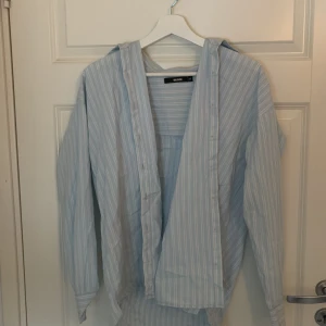 Ljusblå randig skjorta från Bik Bok - Ljusblå skjorta från Bik Bok med vita ränder och lång ärm. Skjortan har en loose passform och är tillverkad i mjuk bomull. Klassisk krage och knappar framtill, perfekt för en chill och stilren look.