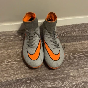 Nike Hypervenom grå/orange fotbollsskor - Säljer ett par Nike Hypervenom fotbollsskor i grått med orange och svarta detaljer Neymar edition. Skorna har högt strumpskaft, snörning och mönstrad sula i orange och svart. Perfekta för dig som vill sticka ut på planen med snygg design och bra grepp.