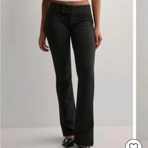  Nelly kostymbyxor - Snygga svarta kostymbyxor med bootcut-snitt och låg midja. Byxorna har två knappar framtill och är perfekta för en trendig och stilren look. Passar dig som gillar klassiska svarta byxor med lite utsvängda ben. 