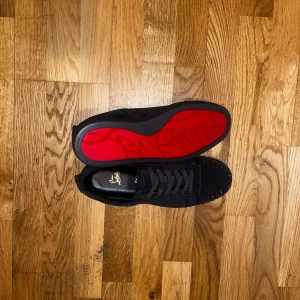 Christian Louboutin gråa sneakers med nitar - Säljer ett par gråa Christian Louboutin sneakers i mocka med coola gråa nitar på tån och klassisk röd sula med logga. Skorna har snörning och rund tå, samt exklusiva detaljer som guldfärgad logotyp på innersulan. Kommer med originalkartong och tillbehör. OBS!! Originalkartong är lite skadad!!
