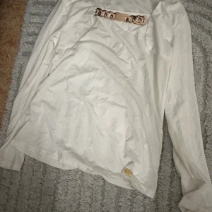 Vit långärmad topp med guldkedja - Snygg vit långärmad topp från Chiara Forthi med en cool guldfärgad kedjedetalj vid halsringningen. Mjuk och skön i bomullsmaterial, perfekt för dig som gillar stilrena plagg med en twist. Passar dig som vill sticka ut lite extra.