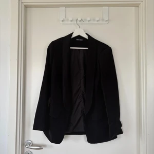 Svart kavaj från SHEIN - Stilren svart kavaj från SHEIN med klassisk krage och två fickor framtill. Rak passform och helfodrad insida. Perfekt för dig som vill ha en enkel och snygg look. Materialet känns mjukt och lätt, vilket gör den bekväm att bära hela dagen.