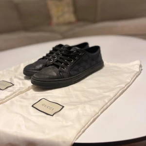 Svarta Gucci skor - Säljer nu dessa Svarta Gucci sneakers med klassisk låg profil och rund tå. Sidorna har diskret GG-monogram i svart och ovandelen är i skinn och textil. Skorna har snörning och platt sula med Gucci-logga undertill. Perfekt för dig som gillar stilrena designer och exklusiva detaljer. Dem är självklart äkta och jag säljer dem nu till ett grymt pris p.g.a några små defekter. Pris är ej hugget i sten. Skriv om det vore några frågor!