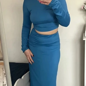 Blå croppad topp och kjol - Säljer en blå långkjol och matchande tröja i stretchigt och mjukt bomull material. Kjolen har en enkel, rak modell utan mönster och sitter högt i midjan. Båda är mycket stretchiga 