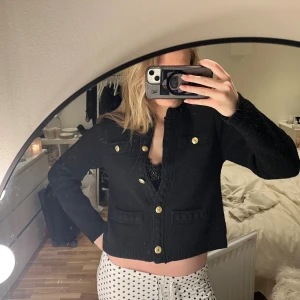 Svart cardigan jacka med guldknappar - Säljer en svart stickad cardigan jacka med snygga guldknappar framtill och på fickorna. Jackan har en lite mer croppad passform på mig som har en lite längre överkropp och vanligtvis har s i tröjor. Långärmade ärmar och två bröstfickor. Perfekt för dig som gillar klassisk men trendig stil.