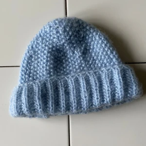 Ljusblå stickad mössa med ribbad kant - Supermysig ljusblå stickad mössa med bred ribbad kant och mjuk, fluffig känsla. Perfekt för kalla dagar och ger en chill vibe till din outfit. Sitter snyggt med lite spetsig form upptill och passar dig som gillar enkel, stilren look.