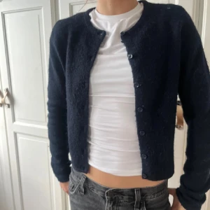 Mörkblå croppad kofta från Ginatricot - Snygg mörkblå kofta från Ginatricot  med croppad passform och rund hals. Koftan är stickad i mjukt material och har långa ärmar samt knappar hela vägen framtill. Perfekt att slänga över en t-shirt för en chill look.