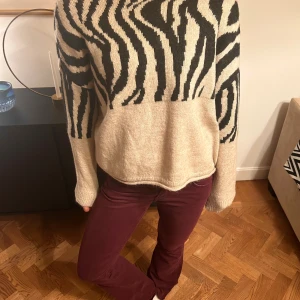 Beige stickad zebramönstrad tröja - Lappen kvar! Säljer en beige stickad tröja med svart zebramönster. Tröjan har en avslappnad passform, rund halsringning och långa ärmar. Perfekt för dig som vill sticka ut med ett coolt djurmönster och ändå hålla det stilrent.