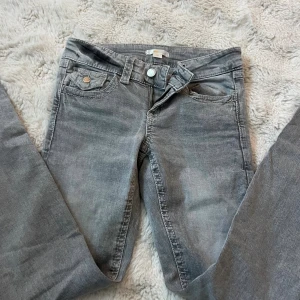 Grå jeans från Gina Tricot - Snygga grå jeans från Gina Tricot i storlek 152. Modellen har bootcut ben, klassiska fem fickor och coola ficklock med knapp bak. Jeansen har dragkedja och knapp framtill, samt bälteshällor. Perfekt för dig som gillar en enkel och stilren look.
