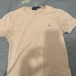 Beige t-shirt Polo Ralph Lauren slim fit - Snygg beige t-shirt från Polo Ralph Lauren i slim fit-modell. Klassisk rund halsringning och broderad logga på bröstet. Tillverkad i mjuk bomull som känns skön mot huden. Perfekt för en clean och stilren look.