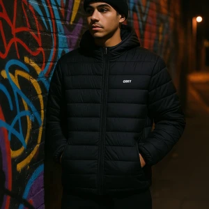 Svart pufferjacka från Obey med huva - Svart pufferjacka från Obey med huva och broderad logga på bröstet. Jackan har quiltad design, två sidofickor med dragkedja och hel dragkedja framtill. Perfekt för kalla dagar och har en clean, modern look som funkar till jeans och sneakers.