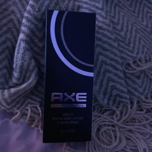 Axe Black Parfym - Axe Black parfym med en stilren design. Text på förpackningen: 'Parfum Bois de Cèdre Intense et Baies Noires'. Perfekt för dig som vill ha en modern och diskret doft.
