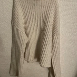 Ribbad krämvit polotröja med breda ärmar - Säljer en supermysig ribbad polotröja i krämvit med breda, långa ärmar och hög krage. Den är använd få gånger, men den kan klia lite.