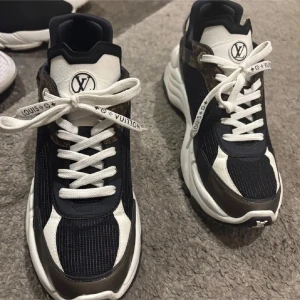 Louis Vuitton sneakers  - Snygga chunky sneakers från Louis Vuitton i svart och vitt med klassiska monogramdetaljer i brunt. Skorna har vit platt sula, rund tå och vita snören med Louis Vuitton-tryck. Materialmix av textil och skinn, samt ikoniska LV-loggor på tunga och häl.