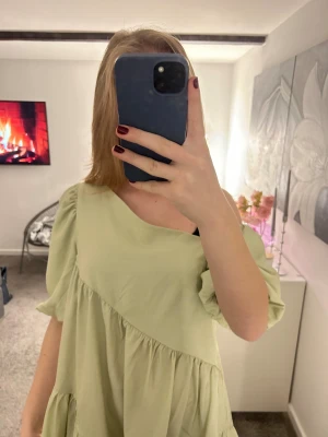 Ljusgrön offshoulder klänning  - Supersöt ljusgrön kortklänning med offshoulder och puffiga korta ärmar. Klänningen har volangdetaljer och en lös, flowy passform som känns riktigt chill. Perfekt för dig som gillar en avslappnad men ändå trendig stil.