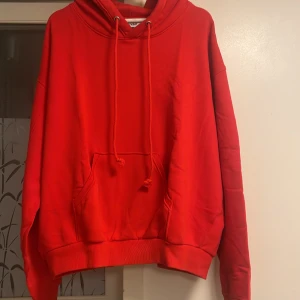 Röd hoodie från Weekday med huva - Säljer en röd hoodie från Weekday i storlek M. Tröjan har en stor huva med snörning, magficka och ribbade muddar vid ärmslut och nederkant. Oversized passform och mjukt bomullsmaterial gör den extra skön. Perfekt för chill dagar eller när du vill sticka ut.