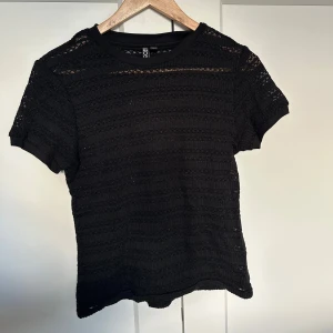 Svart stickad topp från Pieces - Svart stickad topp från Pieces med korta ärmar och rund hals. Toppen har ett genombrutet, virkat mönster i horisontella ränder som ger en luftig känsla. Perfekt att styla med jeans eller kjol för en cool look. Nypris: 300kr. Säljer för: 50kr!