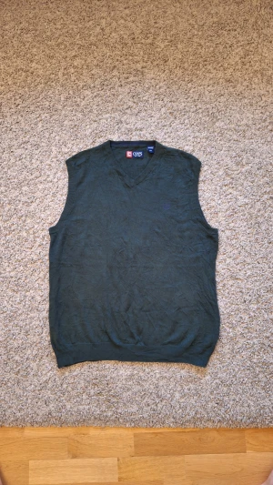 Grön ärmlös stickad tröja från CHAPS - Grön ärmlös stickad tröja från CHAPS i storlek L(passar M också). 100% bomull. Använd fåtal gånger och skicket är i princip som ny, inga slitningar eller defekter finns. Den har en lila logga på vänstra bröstet. Den är varm och skön och passar perfekt nu under julen och vintern! Skick: 9/10