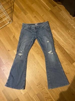 Blå bootcut jeans med slitningar - Säljer ett par blå bootcut jeans med slitna detaljer på låren och snygga broderade bakfickor. Jeansen har låg midja. Jeansen är bara använda en gång och köptes för 399kr