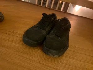 Svarta Vans Old Skool sneakers storlek 38’5 - Svarta Vans Old Skool sneakers med klassisk låg siluett och snörning. Ovandel i mocka och canvas, gummisula med rutigt mönster på insidan. Ikonisk Vans-logga på hälen. Perfekt för dig som gillar streetstyle och skate.