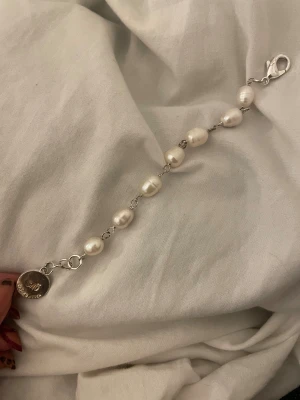 SNO of Sweden pärlarmband silver - Stilrent armband från SNO of Sweden med oregelbundna vita pärlor och silverfärgade länkar. Armbandet har en rund bricka med logga och ett smidigt karbinlås. Perfekt för dig som gillar klassiska detaljer med en modern twist.