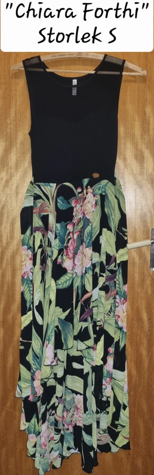 Blommig långklänning Chiara Forthi S - Supersnygg långklänning från Chiara Forthi med svart överdel och blommig kjol i grönt, rosa och vitt. Ärmlös modell med rund halsringning och flowy kjol som ger en riktigt somrig vibe. Perfekt för dig som vill sticka ut med en färgglad och fräsch look.