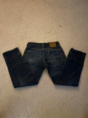Levi's 501 mörkblå jeans W30 L30 - Klassiska Levi's 501 jeans i mörkblå tvätt med raka ben och femficksdesign. Jeansen har den ikoniska läderpatchen bak i midjan och är tillverkade i slitstarkt bomullsjeans. Perfekt för dig som gillar tidlös stil och vill ha ett par riktigt snygga jeans.
