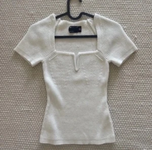 Vit stickad topp från Zara - Säljer en vit stickad topp med korta ärmar och snygg v-ringad hals med unik kant. Modellen är slim och sitter tajt mot kroppen. Perfekt för dig som gillar stilrena och trendiga plagg med lite edge.d n har en liten blå fläck på sig som inte försvinner 