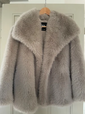 Beige pälsjacka från Zara S - Säljer en fluffig och lyxig beige pälsjacka från Zara i storlek S. Jackan har bred krage och är helfodrad, perfekt för dig som vill ha en statement piece med oversized känsla. Materialet är syntetpäls som ger en mjuk och cool look.