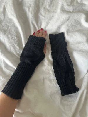 Svarta stickade fingerlösa handskar - Svarta, ribbstickade fingerlösa handskar som går upp över handleden. Perfekta för dig som vill ha värme men ändå kunna använda mobilen eller fixa med grejer. Mjukt stickat material och enkel, clean design