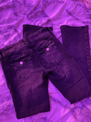Svarta jeans med bootcut - Snygga svarta jeans med bootcut och dubbla knappar fram. Baksidan har fickor med lock och knappdetalj. Jeansen har klassisk femficksdesign och är tillverkade i mjukt denimtyg som sitter skönt hela dagen.